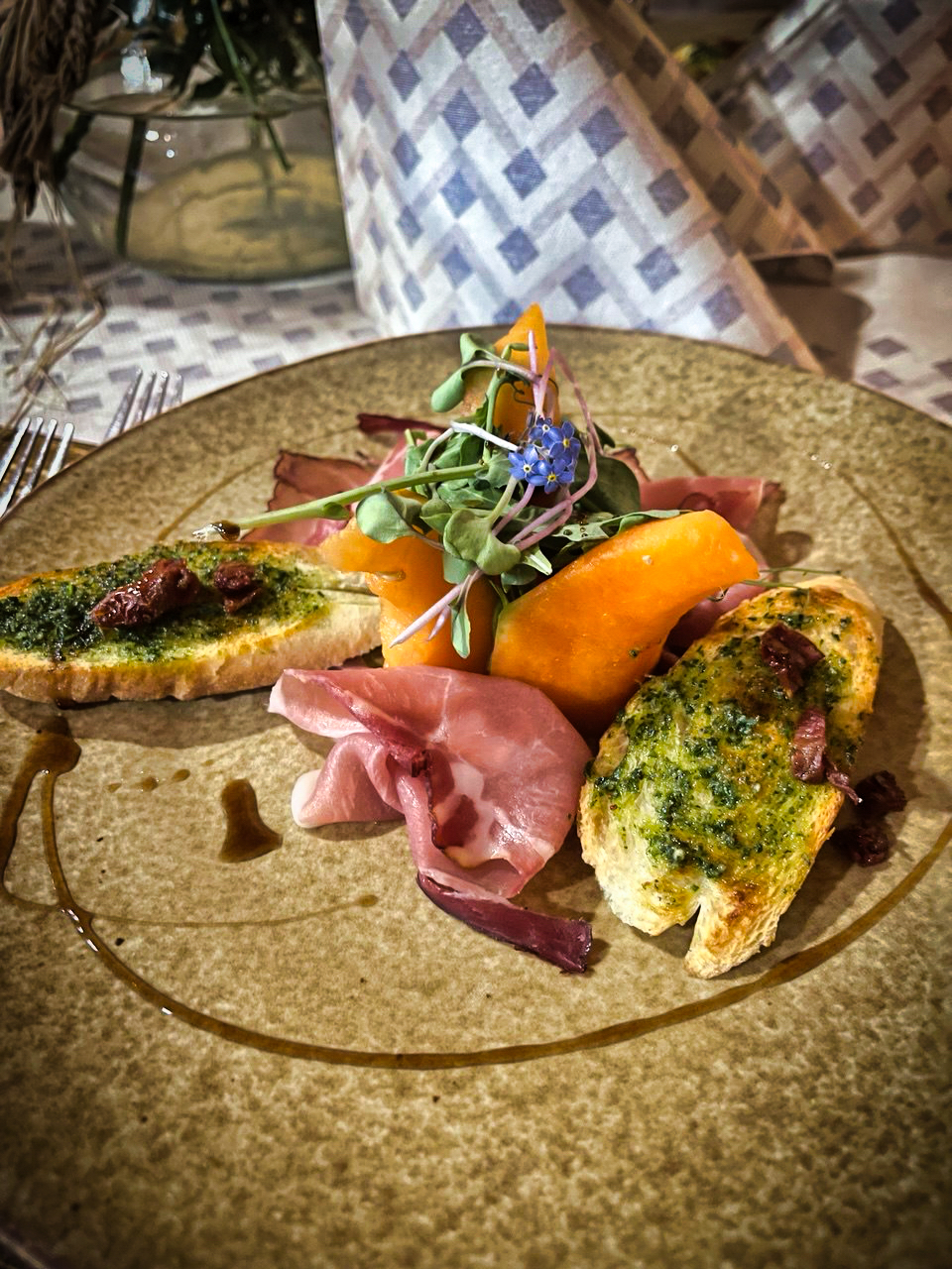 Umelecky podaný predkrm s prosciuttom, persimónom, bylinkovým chlebom a jedlými kvetmi