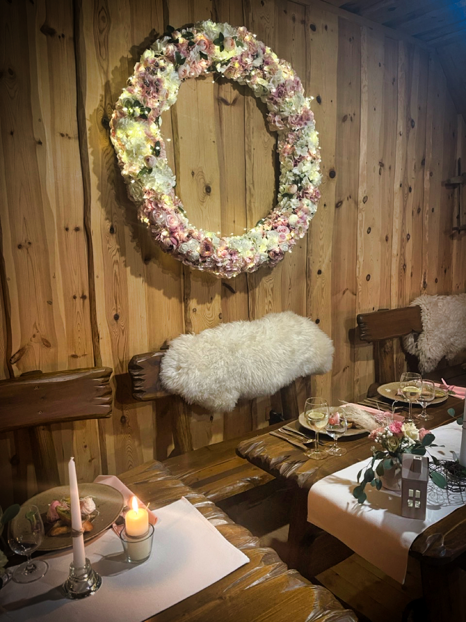 Romantická jedáleň s veľkým kvetinovým vencom, sviečkami a ovčími kožušinami